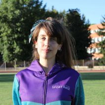 Ritratto di una giovane donna che indossa una tuta viola Sport Race, in piedi su un campo sportivo. {{brizy_dc_image_alt imageSrc=